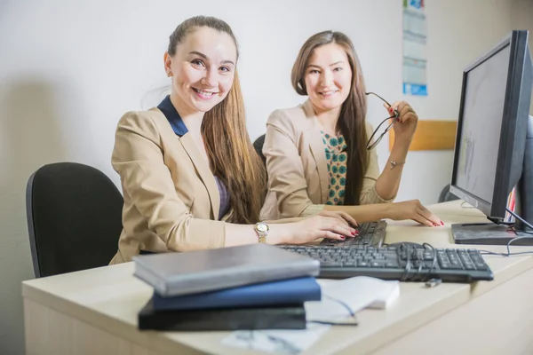 Two girl students are sitting at the computer in the office
