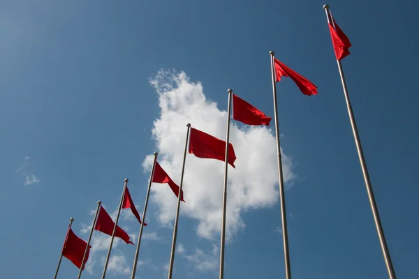 Line of red flags in front of cloudy blue sky