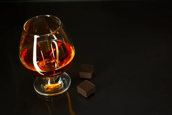 Brandy glass and chocolate on black background