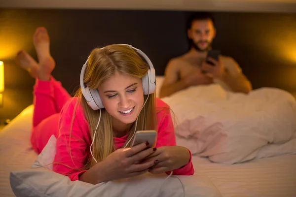 Young women on bed using mobile phone with headphones