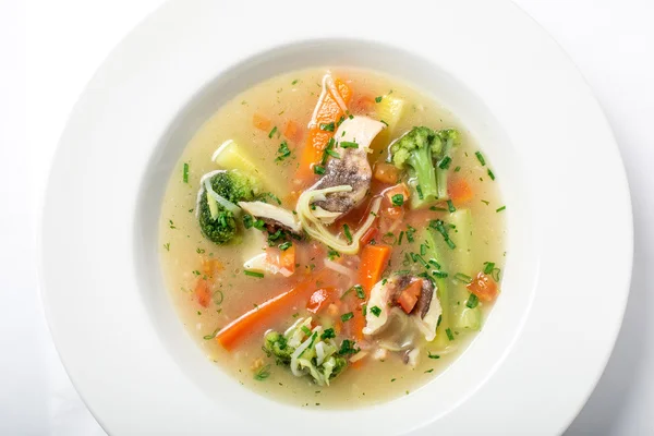 Light fish soup with vegetables and broccoli in white plate.