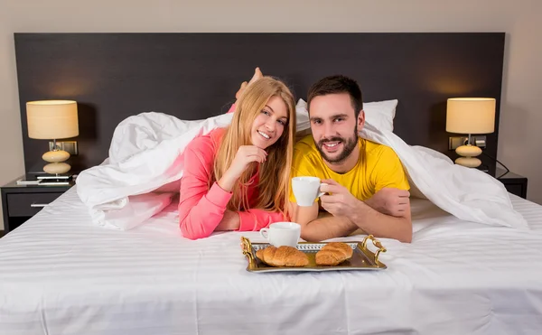 Happy young couple having breakfast tray on bed at home