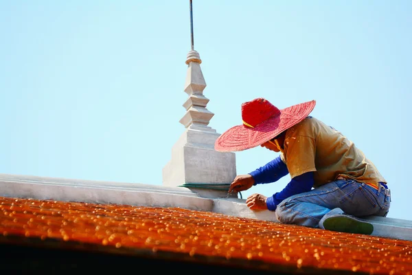 Construction worker on a roof covering it with tiles ( Thai style).