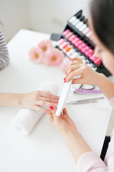 Woman in salon receiving manicure by nail beautician