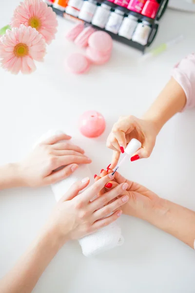 Woman in salon receiving manicure by nail beautician