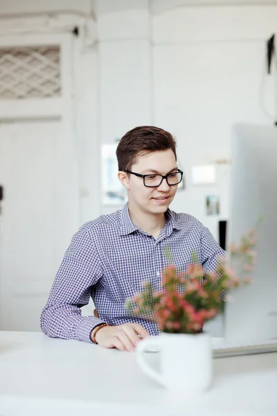 Happy young man, wearing glasses and smiling, as he works on his laptop