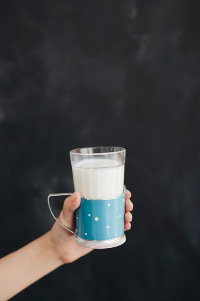 Woman hand keeps the glass with milk on black background