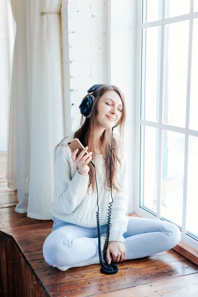 Woman listening music in headphones on windowsill background