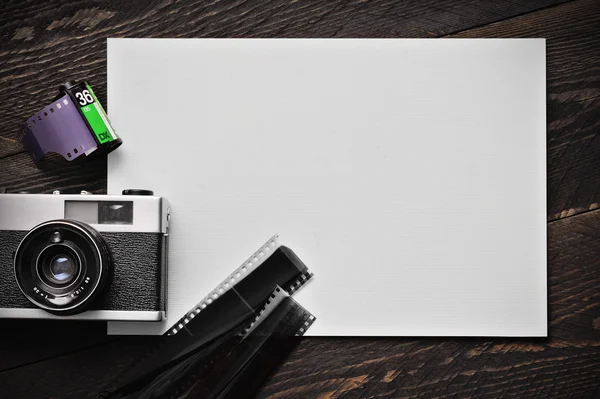 Vintage old photographic film sing lens camera with a film roll and film strip on a white paper on a darkness wooden background