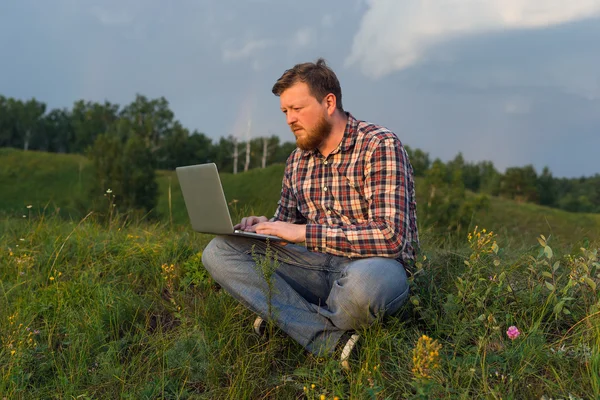 Man sitting on the grass with a laptop on his knees.