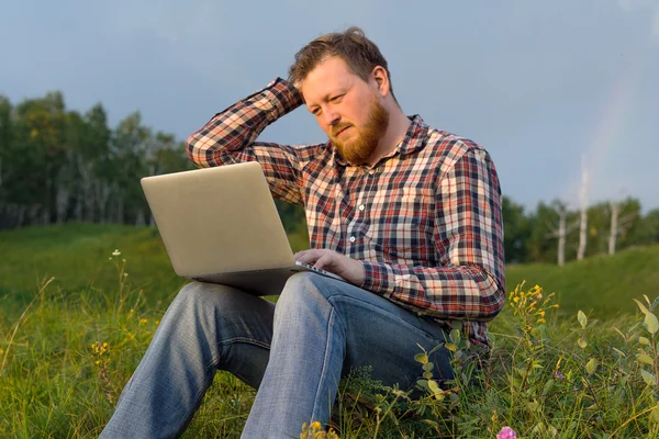 Man sitting on the grass with a laptop on his knees.