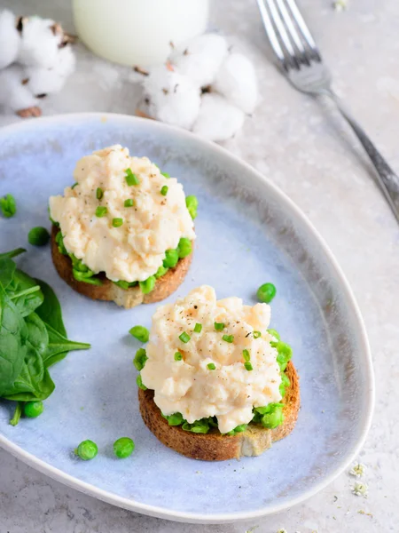 Scrambled eggs with peas on toasts