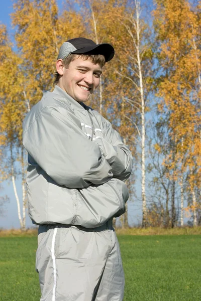 A guy in a tracksuit in front of the yellow foliage of trees