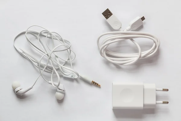 White smartphone charger, USB Cable and white earphones on a white background.