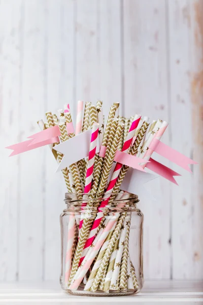 Striped mixed gold and pink drink straws in a glass jar with a sticker on a light wood background