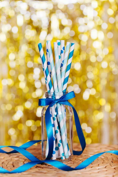 Blue paper drink straws to celebrate a party on shiny gold blurred background closeup