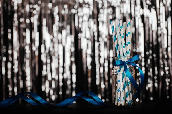 Striped mixed blue and white paper drink straws in jar on  silver blurred background with black shiny bokeh