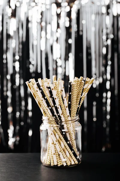 Striped mixed gold, black and white paper drink straws in jar on blurred background with black shiny bokeh