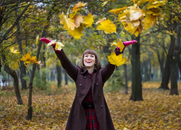 Young woman playing with leaves in autumn park