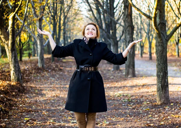 Happy young woman raising hands in autumn park