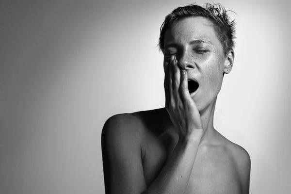 Portrait of white young woman yawn, face with freckles, monochrome dark background