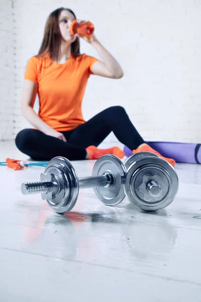 Sport fit woman posing and drink water in a gym with equipment, dumbbell and training pad