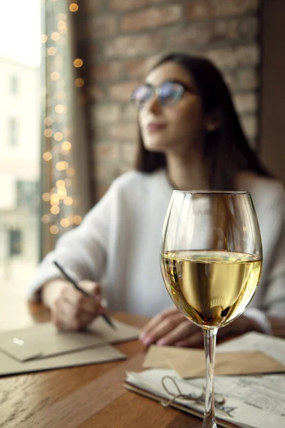 Portrait of a beautiful young woman drink white wine and having rest in cafe near window