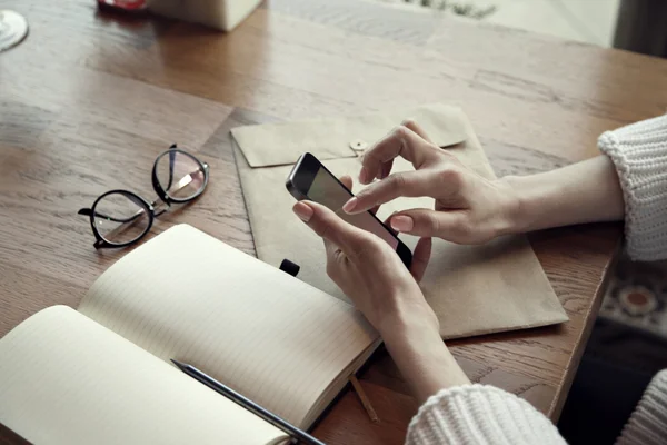 Close-up view of woman hands with phone and note pad, glasses, in cafe