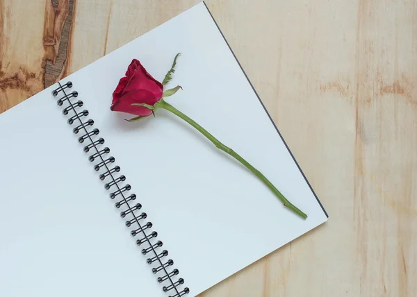 Red rose with a note book on wood background
