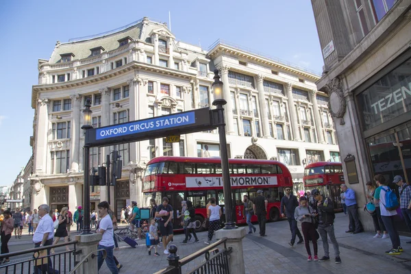 Red bus passing by oxford circus underground station with tourist walking around