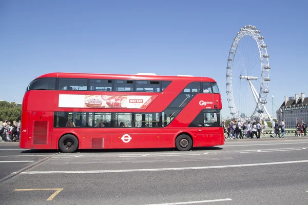 Red london bus drives over westminster bridge with london eye in