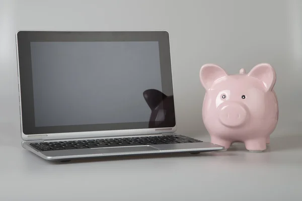 Pink piggy bank next to tablet, laptop