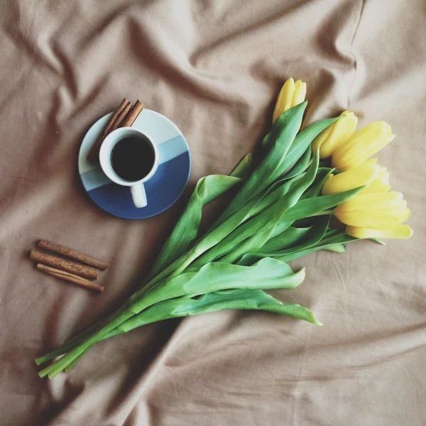 Cup of coffee, cinnamon and yellow tulips