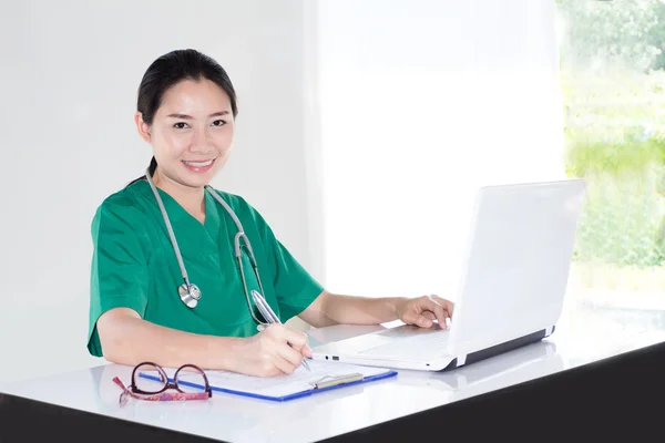 Woman doctor in green uniform working with computer and writing