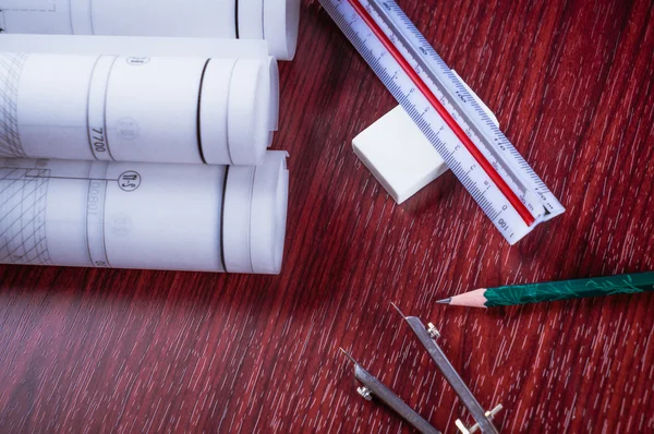 Architectural blueprints and blueprint rolls and a drawing instruments on the worktable