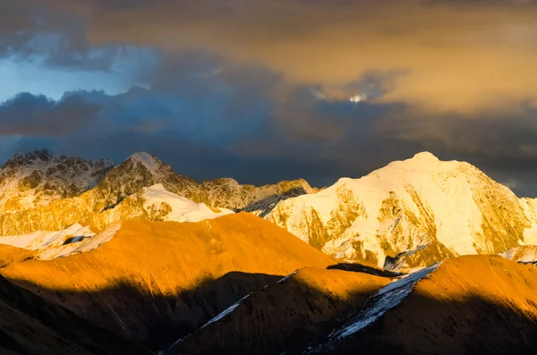 View from St. Moritz in Switzerland: high snow and ice capped alpine mountain range with red illuminated peaks at sunset and the moon out