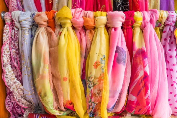 The multi-colored scarves hanging on a wooden hanger.