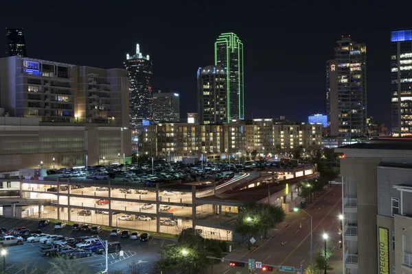 Lights of the Dallas skyline beyond a lit up parking garage