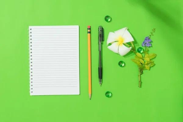 Empty sheet of notepad with pen, pencil and frangipani flower on green background for some idea or message