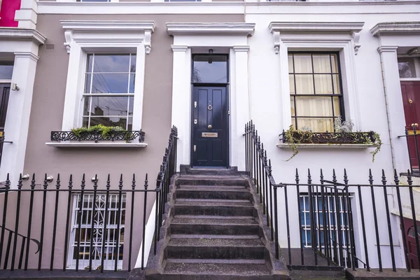 Brown and white typical colorful houses with stairs and black door at Notting Hill district, near Portobello road - London, UK