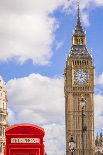 Classic red British telephone box with the Big Ben at background on a sunny afternoon with blue sky and clouds - London, UK