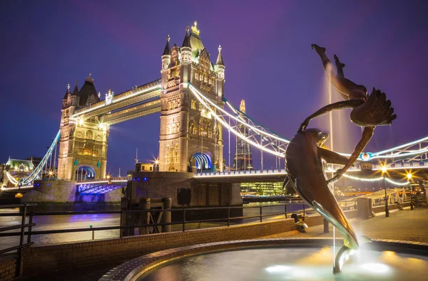 The lady and the dolphin fountain with Tower Bridge at night, London, UK