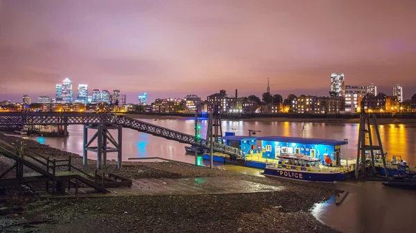 Police station on the river Thames with Canary Wharf at night, London, UK