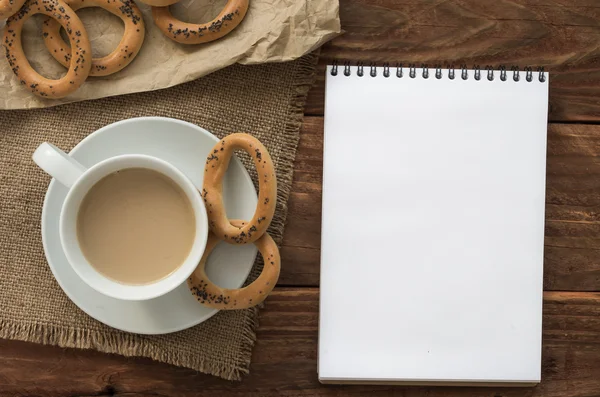 Top view office workplace: white notepad with bagels and coffee on the wooden table.