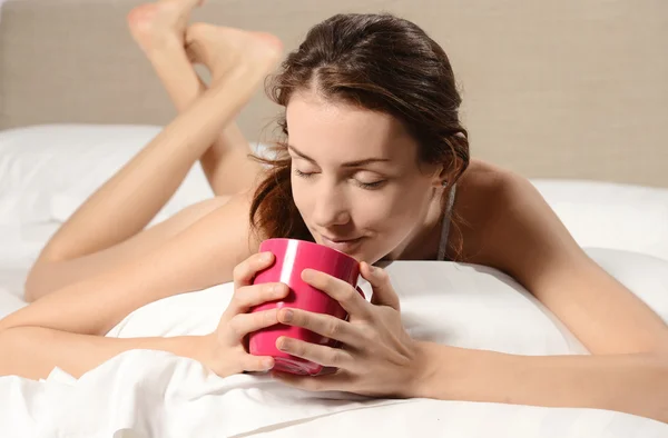 Beautiful young woman in the bed with pink cup