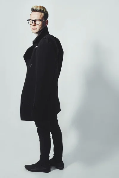 Fashion portrait of young man in black shirt poses over wall with contrast shadows