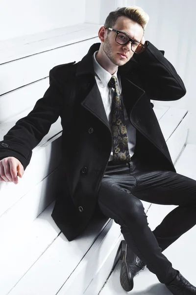 Fashion portrait of young man in black shirt poses over wall with contrast shadows