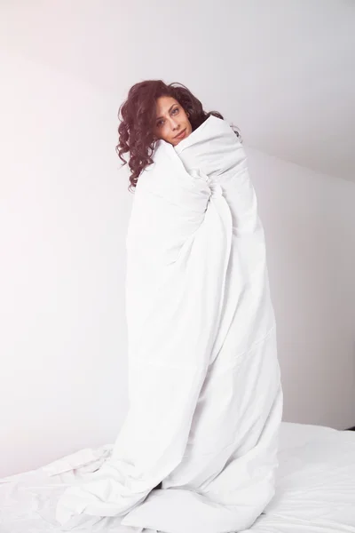 Brunette woman covered by white duvet on hite bed