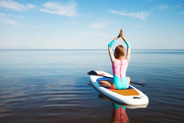 Woman doing yoga on sup board with paddle