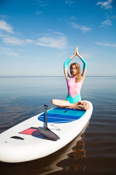 Woman doing yoga pranayam on sup board with paddle